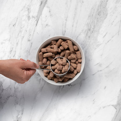 hand scooping from a white bowl of NRG Freeze Dried Beef Cat Food